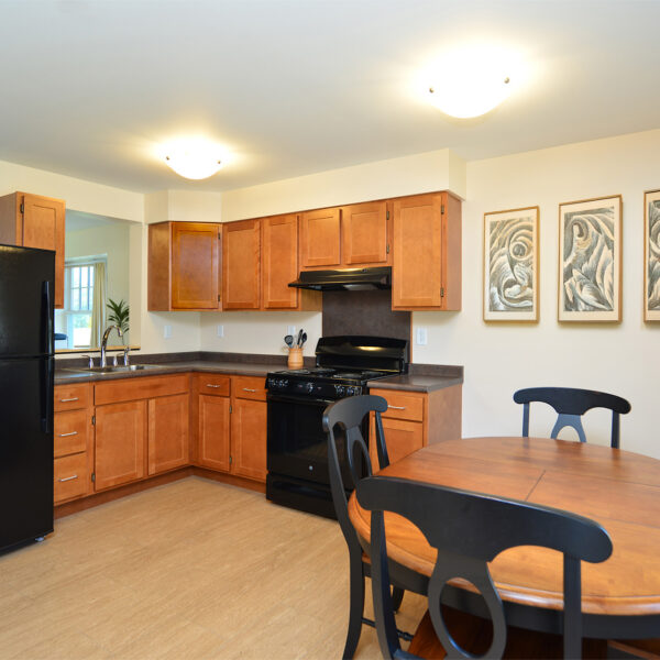Modern kitchen with wooden cabinets, black appliances, and a round dining table with black chairs.