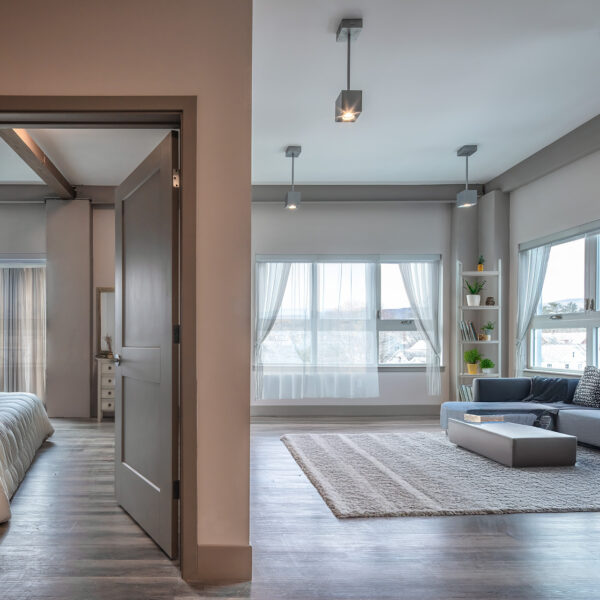 Modern living room with gray sectional, coffee table, large windows, and view into adjacent bedroom.