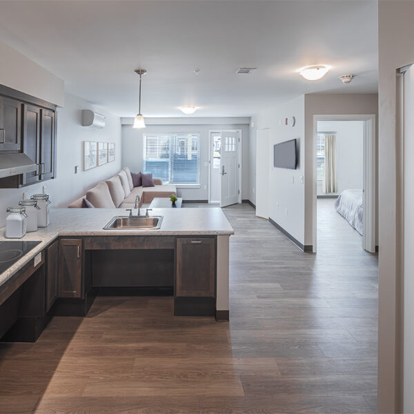 Open-concept apartment with modern kitchen, marble island, stainless appliances, and bright living room with large windows.
