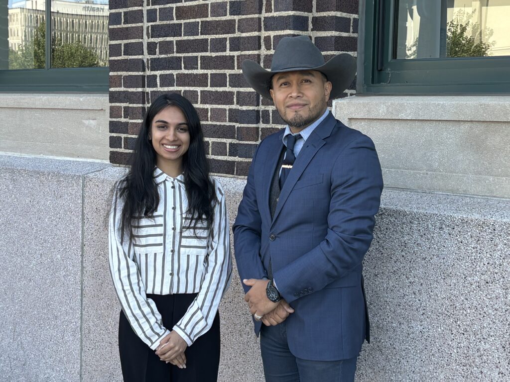 A woman in a striped shirt and a man in a blue suit with a cowboy hat standing in front of a building,