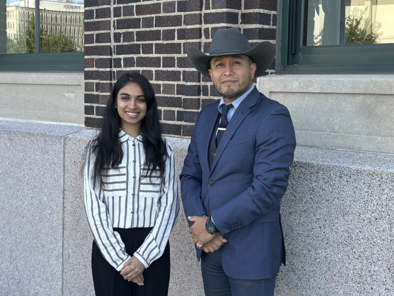 A woman in a striped shirt and a man in a blue suit with a cowboy hat standing in front of a building,