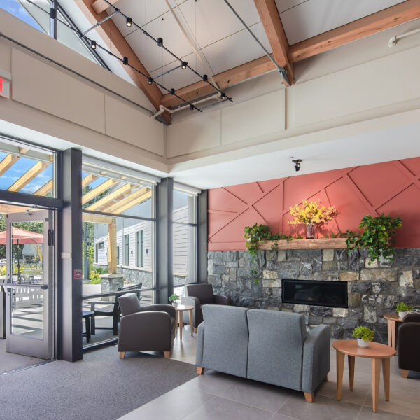 Cozy indoor seating area with stone fireplace, wooden beams, string lights, and large windows to outdoor patio.