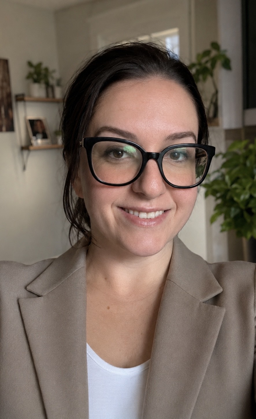 headshot of woman with brown hair and glasses in a tan suit jacket
